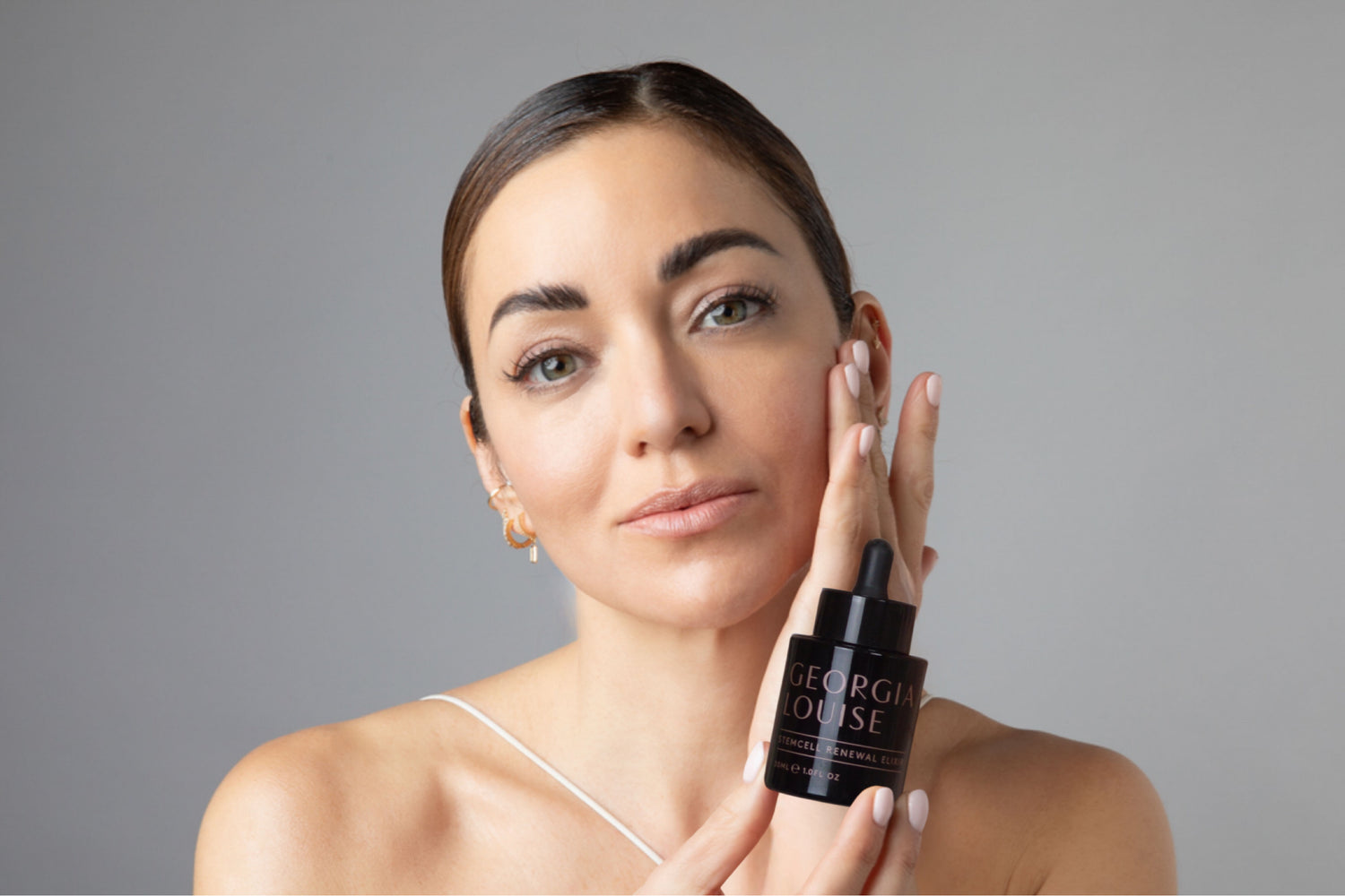 Person holding a bottle of skincare serum, looking at the camera