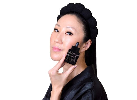 Woman holding a skincare product with a confident expression.