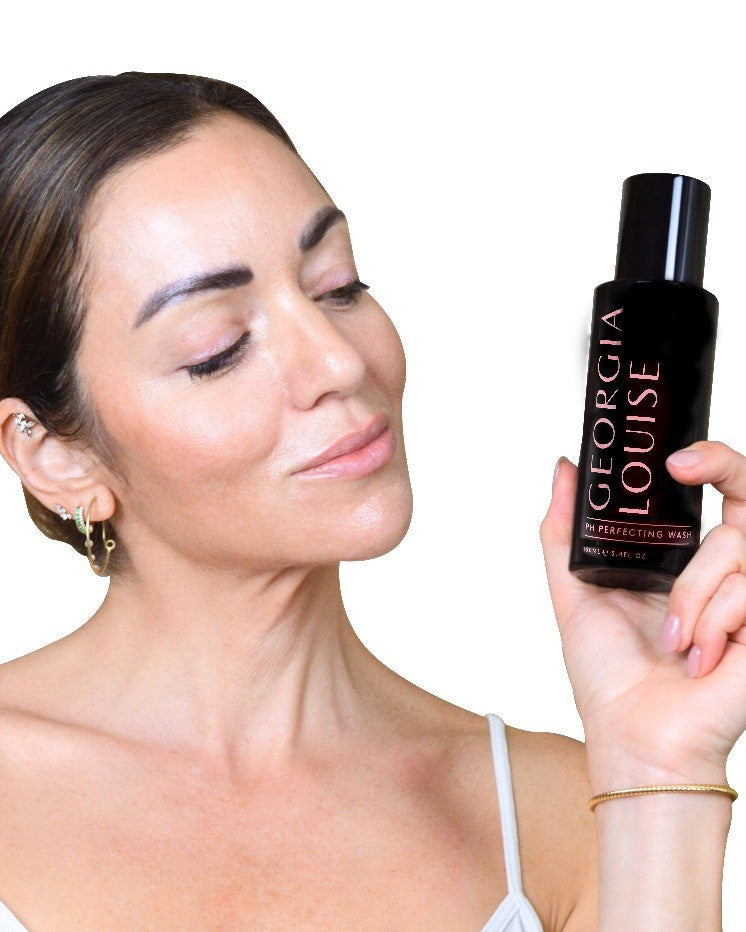 Woman holding a bottle of Georgia Louise skincare product and smiling