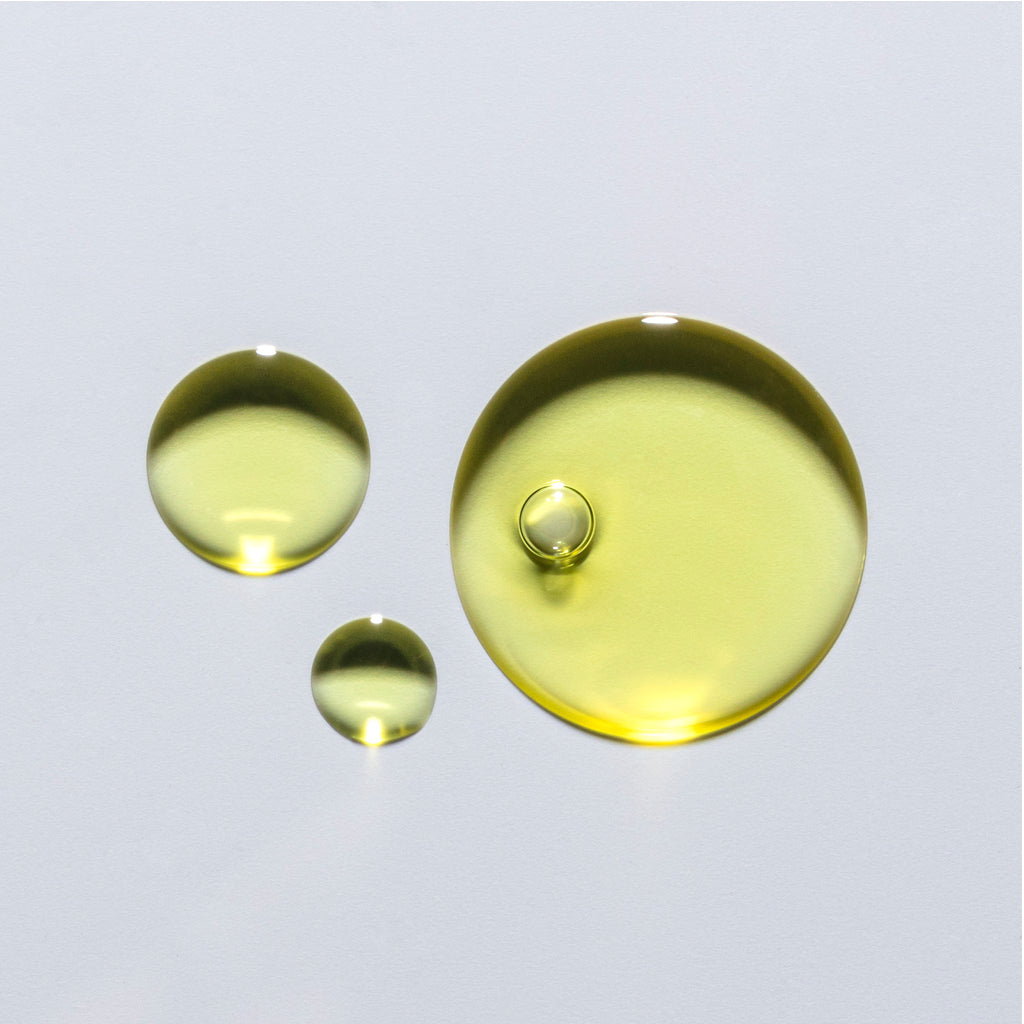 Three droplets of yellow oil on a light background.